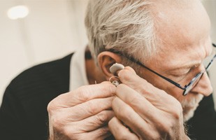 Senior man placing hearing aid in ear