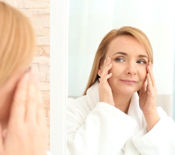 Woman looking in mirror, wondering if she should get dermal fillers