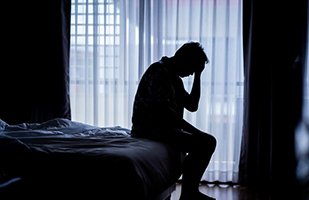 Silhouette of exhausted man sitting on bed