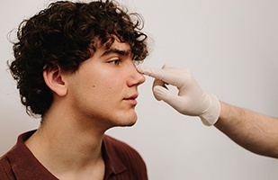 Gloved hand touching young man’s nose