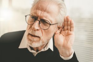 Older man in dark sweater struggling with hearing loss