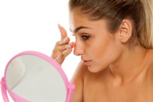 Concerned woman looking at her nose in mirror 