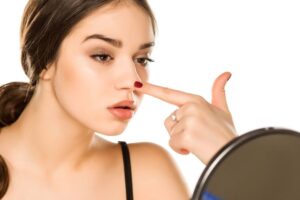 Woman looking at her nose in mirror, wearing contemplative expression 