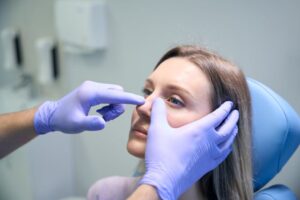 Gloved hands touching a woman’s face during rhinoplasty consultation 